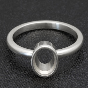 May include: A silver ring with an oval setting. The ring band is thin and circular, leading to the central setting. The setting is designed to hold a gemstone or other decorative element. The ring is shown against a dark background.