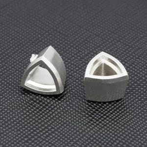 May include: A pair of silver triangle shaped earrings. The earrings are hollow and have a geometric design.