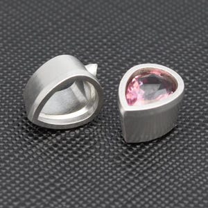 May include: Two silver teardrop-shaped pendants, one with a pink gemstone set in the centre.