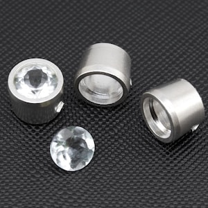 May include: Three silver settings for a jewelry making project. Each setting has a round bezel and a clear crystal stone.