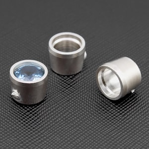 Könnte beinhalten: Drei silberne Ringfassungen aus Metall, eine mit einem hellblauen Edelstein.