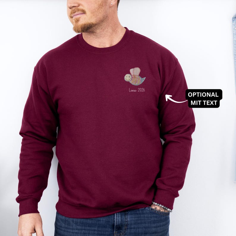 May include: Burgundy crewneck sweatshirt with a small bee graphic and the text "Luna 2026" on the chest. The bee is in shades of brown, blue, and yellow. The sweatshirt is a solid color and has long sleeves.