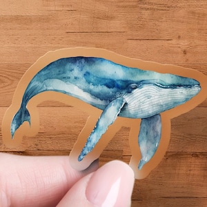 May include: A blue watercolor whale sticker on a wood background.