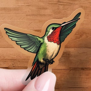 May include: A clear sticker with a detailed illustration of a hummingbird with green and red feathers. The hummingbird is in flight with its wings spread out.