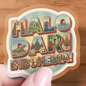 May include: A sticker with the text "HALO DARI INDONESIA!" in a retro style. The sticker features illustrations of Indonesian landmarks, including temples, rice fields, and an orangutan. The sticker is held by a person.