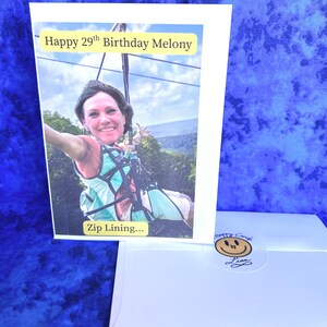 May include: A birthday card with a photo of a person zip lining. The card reads "Happy 29th Birthday Melony" and "Zip Lining...". A white envelope with a smiley face sticker is also visible.