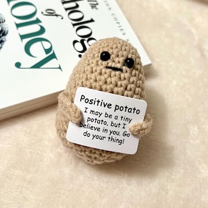May include: A handmade crochet potato character with a sign saying "Positive potato" next to a book titled "The Psychology of Money". The potato has black button eyes and a stitched mouth.