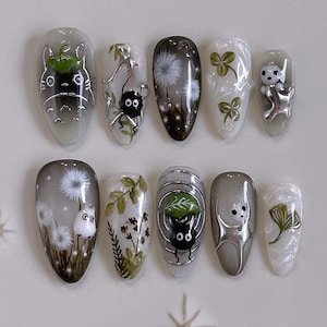 Puede incluir: Un juego de diez uñas postizas con diseños detallados pintados a mano que incluyen un espíritu del bosque gris, duendes del hollín negros, dientes de león blancos, tréboles verdes, pequeñas criaturas blancas y follaje verde sobre una base neutra.
