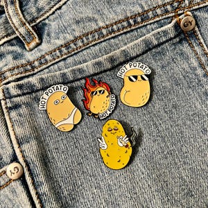 Peut inclure: Quatre épingles en émail représentant des pommes de terre en dessin animé avec le texte "Hot Potato" sur un fond en jean bleu. Les pommes de terre portent des lunettes de soleil, un chapeau de chef et l'une d'elles fume une cigarette.