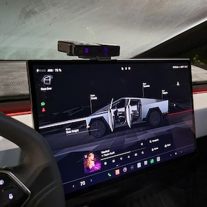 May include: A white Tesla Cybertruck is displayed on the touchscreen of a Tesla vehicle. The touchscreen shows the Cybertruck's dimensions and features, including the front, rear, and side profiles. The touchscreen also displays the vehicle's current speed, which is 70 mph.