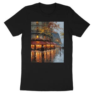 May include: Black t-shirt featuring a painting of a rainy Parisian street scene. The artwork depicts a cafe with red awnings, warm interior lights, and reflections on the wet pavement. A tree with autumn leaves and buildings are in the background.