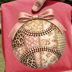 Peut inclure: Une balle de baseball décorative avec un motif patchwork floral, léopard et à carreaux. La balle est ornée d'un nœud en satin et tenue sur un fond rose.