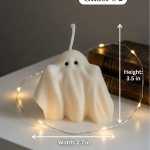 K&ouml;nnte beinhalten: Eine cremefarbene, geisterf&ouml;rmige Kerze mit zwei schwarzen Augen und einem wei&szlig;en Docht. Die Kerze ist mit Ghost #2 beschriftet und zeigt Messpfeile f&uuml;r eine H&ouml;he von 3,5 Zoll und eine Breite von 2,7 Zoll, umgeben von einer d&uuml;nnen Lichterkette.