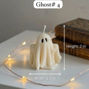 K&ouml;nnte beinhalten: Eine cremefarbene, geisterf&ouml;rmige Kerze mit zwei schwarzen, ovalen Augen und einem wei&szlig;en Docht. Die Kerze ist mit Ghost# 4 beschriftet und misst 2 Zoll in der H&ouml;he und 1,5 Zoll in der Breite. Ein d&uuml;nner Draht mit kleinen warmen LED-Lichtern umgibt die Kerze.