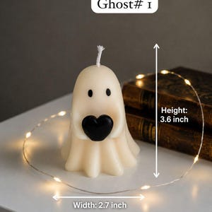 K&ouml;nnte beinhalten: Eine cremefarbene, geisterf&ouml;rmige Kerze mit zwei schwarzen Augen, die ein schwarzes Herz h&auml;lt. Die Kerze hat einen wei&szlig;en Docht an der Oberseite. Der Text auf dem Bild lautet Ghost# 1, Height: 3.6 inch und Width: 2.7 inch f&uuml;r die Ma&szlig;e.