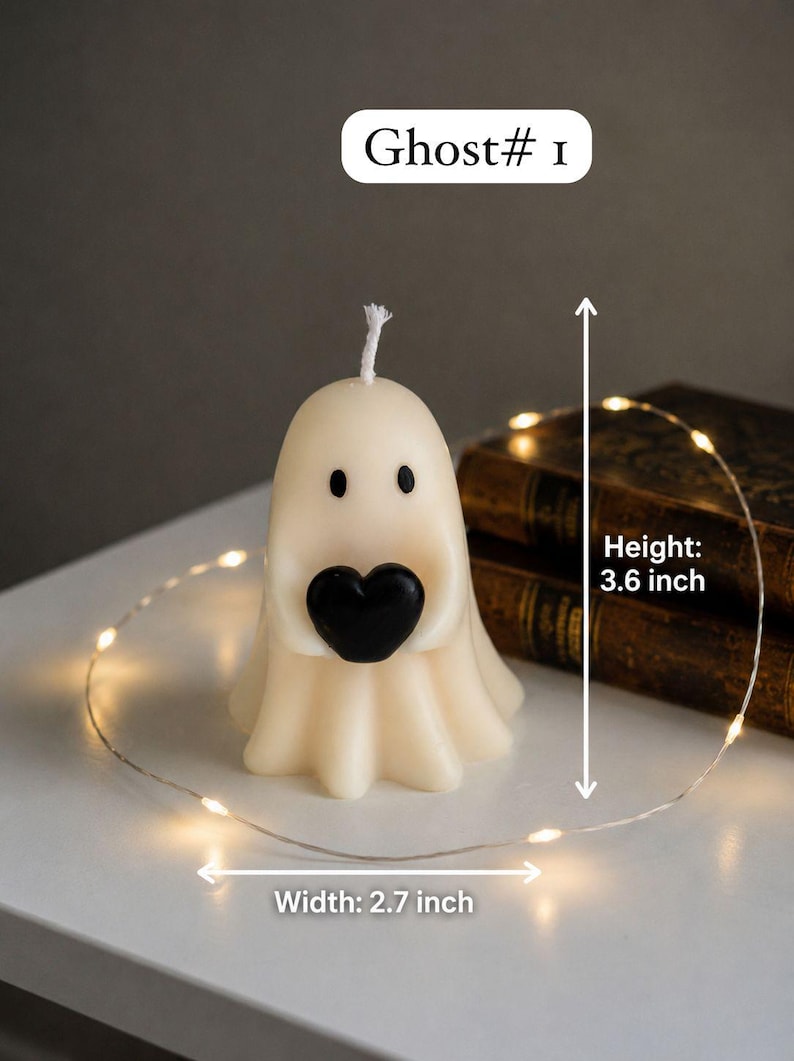 K&ouml;nnte beinhalten: Eine cremefarbene, geisterf&ouml;rmige Kerze mit zwei schwarzen Augen, die ein schwarzes Herz h&auml;lt. Die Kerze hat einen wei&szlig;en Docht an der Oberseite. Der Text auf dem Bild lautet Ghost# 1, Height: 3.6 inch und Width: 2.7 inch f&uuml;r die Ma&szlig;e.