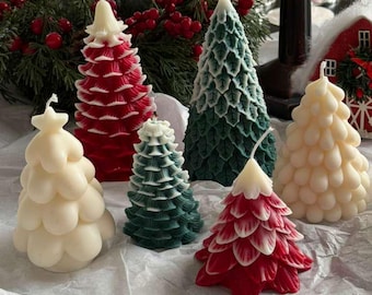 May include: A collection of Christmas tree-shaped candles in various colors, including red, green, and cream. The candles are arranged on a white surface, with a festive background of greenery and berries. The candles vary in size and design.