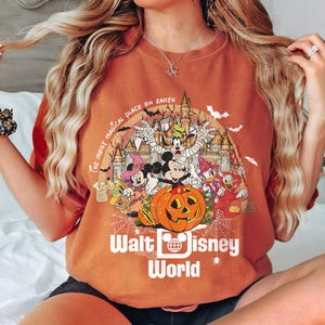 May include: Orange t-shirt with a graphic of Mickey Mouse and friends dressed in Halloween costumes in front of a castle. The text "The Most Magical Place on Earth" and "Walt Disney World" are printed on the shirt.