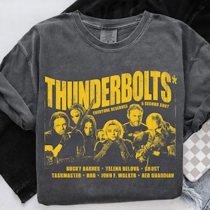 May include: Dark gray crew neck sweatshirt with the word "THUNDERBOLTS" in yellow, along with character images and text. The text "EVERYONE DESERVES A SECOND SHOT" is also present. The names Bucky Barnes, Yelena Belova, Ghost, Taskmaster, Bob, John F. Walker, and Red Guardian are listed.