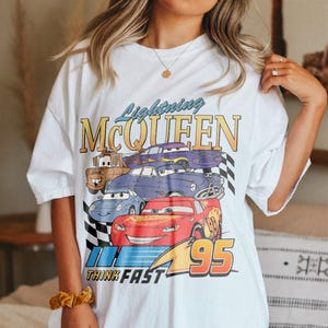 May include: White oversized t-shirt with a graphic print of Lightning McQueen and other Cars characters. The graphic includes the text "Lightning McQueen", "Think Fast", and "95".