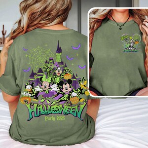 Op de afbeelding: Olijfgroen Halloween Party 2025 t-shirt met een griezelig ontwerp met stripfiguren, een spookkasteel, vleermuizen en het woord "Halloween" in groen en paars. De voorkant van de shirt heeft een skelet karakter met het woord "BOO!" en "Custom Name".