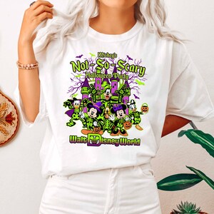 May include: White t-shirt featuring a graphic for Mickey's Not-So-Scary Halloween Party at Walt Disney World. The design includes Disney characters in skeleton costumes, a castle, and the event's name in green and purple.