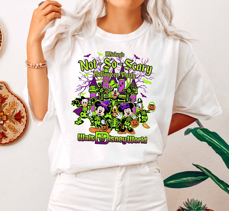 May include: White t-shirt featuring a graphic for Mickey's Not-So-Scary Halloween Party at Walt Disney World. The design includes Disney characters in skeleton costumes, a castle, and the event's name in green and purple.