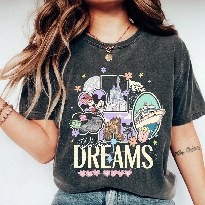 May include: Dark gray t-shirt featuring a colorful graphic with the text "What Dreams". The graphic includes images of a cruise ship, a castle, and Mickey and Minnie Mouse. The shirt has a vintage, worn look.