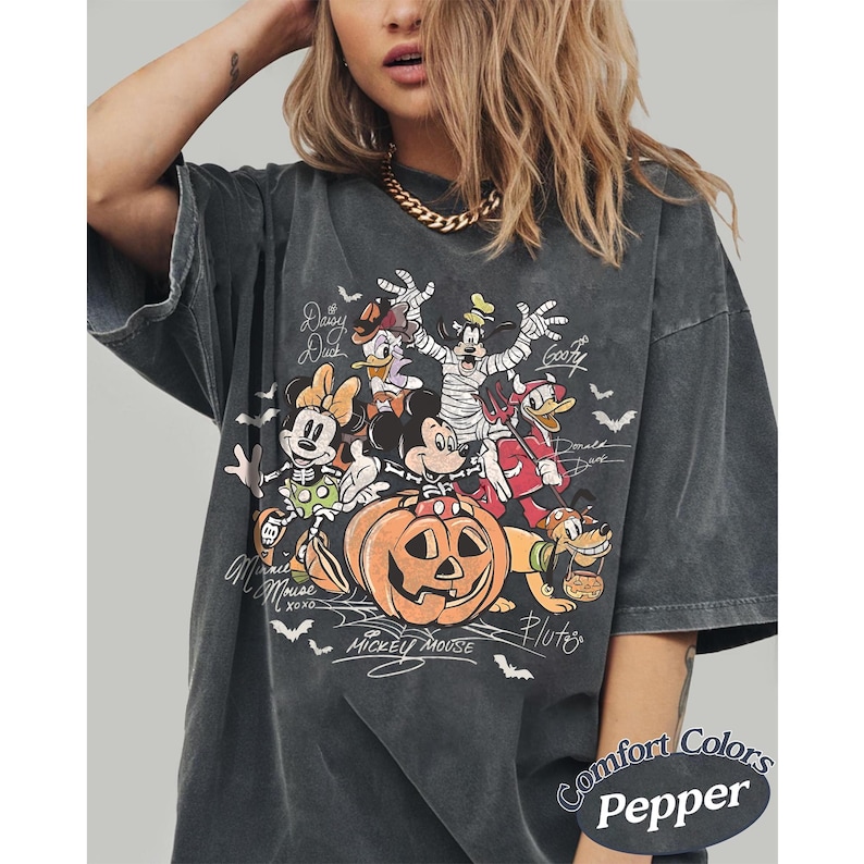 May include: A charcoal gray t-shirt featuring a Halloween-themed graphic of Disney characters including Mickey Mouse, Minnie Mouse, Donald Duck, Daisy Duck, Goofy, and Pluto. The characters are dressed in costumes around a large orange pumpkin.