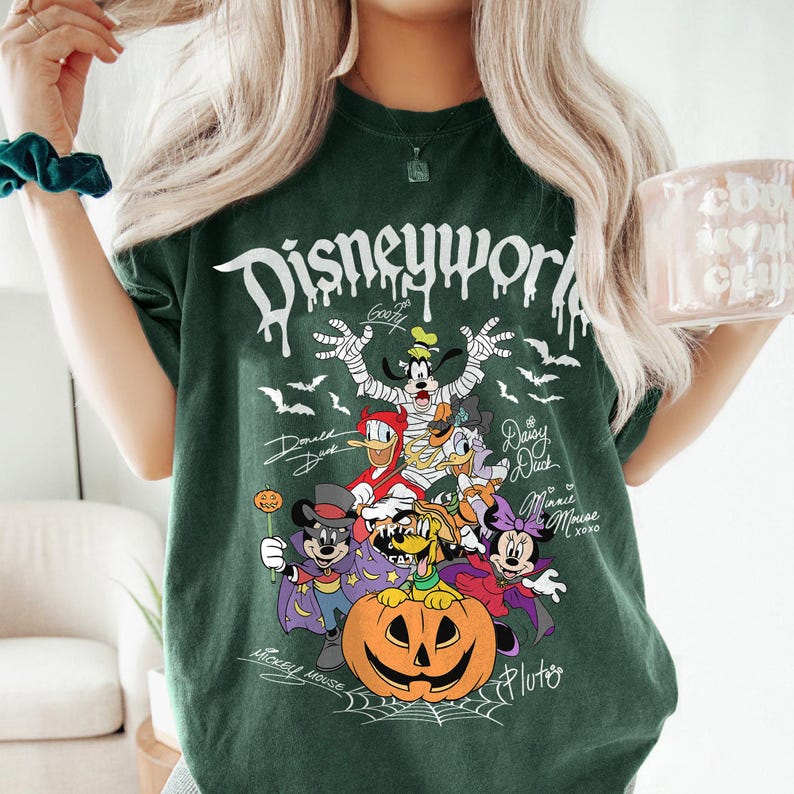 May include: Dark green t-shirt with a Halloween-themed Disney World graphic. The design features various Disney characters dressed in Halloween costumes, including Mickey Mouse, Donald Duck, and Goofy, with the text "Disneyworld" in a dripping font.