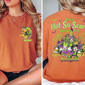 May include: Orange t-shirt featuring a Halloween-themed design. The front displays a cartoon character with a pumpkin and the word "NAME". The back has the text "Mickey's Not-So-Scary Halloween Party Disneyland" with cartoon characters and a castle.