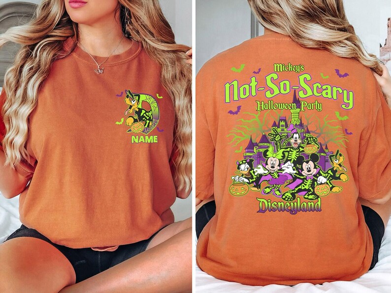 May include: Orange t-shirt featuring a Halloween-themed design. The front displays a cartoon character with a pumpkin and the word "NAME". The back has the text "Mickey's Not-So-Scary Halloween Party Disneyland" with cartoon characters and a castle.