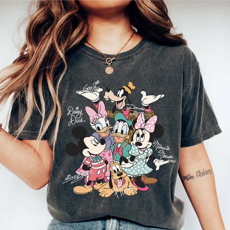 May include: Dark gray t-shirt featuring a colorful graphic of Disney characters including Mickey Mouse, Minnie Mouse, Donald Duck, Daisy Duck, Goofy, and Pluto. The shirt has the names of the characters written in cursive.