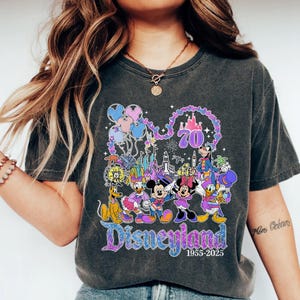May include: Dark gray t-shirt featuring a colorful Disneyland graphic. The design includes Mickey and Minnie Mouse, Donald Duck, Goofy, and Pluto, along with the Disneyland logo and the years 1955-2025. The number 70 is also featured in the design.