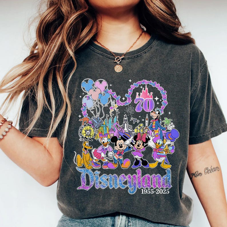 May include: Dark gray t-shirt featuring a colorful Disneyland graphic. The design includes Mickey and Minnie Mouse, Donald Duck, Goofy, and Pluto, along with the Disneyland logo and the years 1955-2025. The number 70 is also featured in the design.