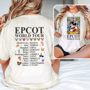 Pode incluir: Camiseta branca com um gr&aacute;fico de Mickey Mouse e outros personagens da Disney em frente a um mapa mundial colorido. O texto "EPCOT WORLD TOUR" est&aacute; impresso na camiseta. A parte de tr&aacute;s da camiseta tem uma lista de pa&iacute;ses e cidades com &iacute;cones que representam cada local.
