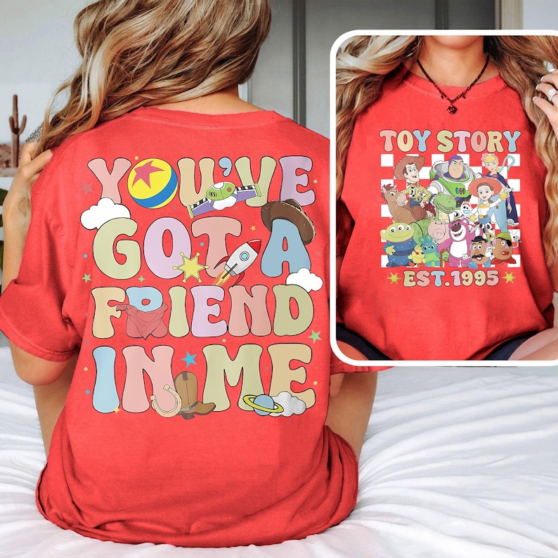 May include: Red t-shirt with a colorful graphic that says "You've Got a Friend in Me" with Toy Story characters. The front of the shirt has a checkered pattern with the text "Toy Story Est. 1995" and a group of Toy Story characters.