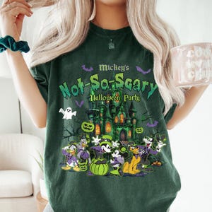 May include: Dark green t-shirt featuring a Halloween design with the text "Mickey's Not-So-Scary Halloween Party." The graphic includes a haunted castle, pumpkins, bats, and cartoon characters.