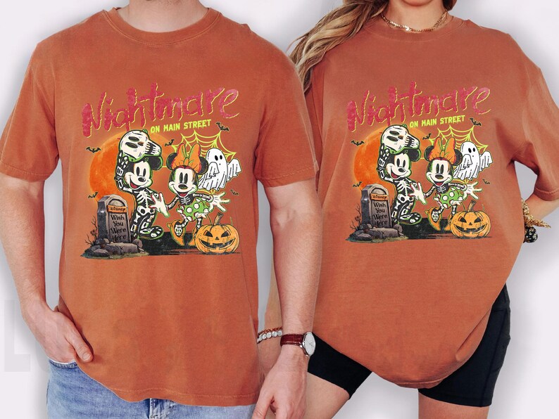 May include: Burnt orange t-shirts featuring a Halloween-themed graphic. The design includes Mickey and Minnie Mouse dressed as skeletons, a pumpkin, and the text "Nightmare on Main Street."