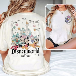 May include: White t-shirt with a graphic of Mickey Mouse and friends in front of Cinderella's Castle. The text "Disneyworld 2025 Trip" is printed below the graphic. The back of the shirt has a graphic of a cartoon character with the text "Sister".