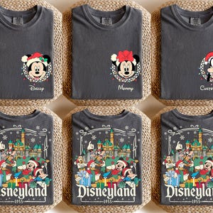 May include: Six dark gray t-shirts with Disney character designs. Three shirts feature Mickey, Minnie, and Goofy with Christmas lights and text. The other three shirts display a Disneyland design with characters and the text "Disneyland 1955".