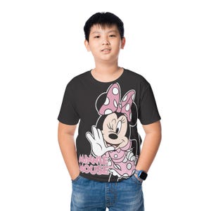 May include: Black t-shirt featuring a Minnie Mouse graphic. The design includes Minnie's face, a pink polka-dot bow, and the words "MINNIE MOUSE" in pink. The shirt is worn by a person in blue jeans.