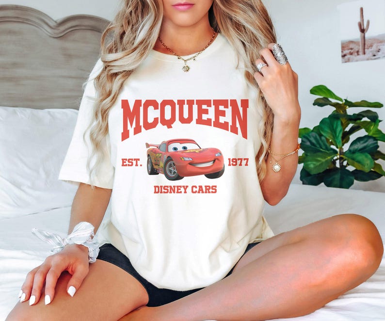Puede incluir: Camiseta blanca con un gr&aacute;fico rojo de Rayo McQueen de Cars de Disney. El texto "MCQUEEN EST. 1977 DISNEY CARS" est&aacute; impreso en la camiseta.