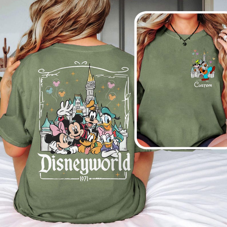 May include: An olive green t-shirt with a Disney castle and character graphic, and the text "Disneyworld 1971." A smaller graphic of the characters is on the front. The shirt is a relaxed fit, casual style.