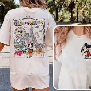 Op de afbeelding: Cr&egrave;mekleurig T-shirt met een Disney World-afbeelding op de achterkant met Mickey Mouse, Minnie Mouse, Donald Duck en andere personages. De voorkant van het shirt heeft een kleine Mickey Mouse-afbeelding en het woord "Daddy".