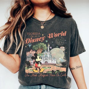 May include: Dark gray t-shirt featuring a colorful graphic of Disney World in Florida. The design includes Mickey Mouse, Cinderella's castle, and the text "Florida Disney World Est. 1971" and "The Most Magical Place On Earth."