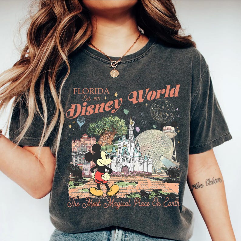 May include: Dark gray t-shirt featuring a colorful graphic of Disney World in Florida. The design includes Mickey Mouse, Cinderella's castle, and the text "Florida Disney World Est. 1971" and "The Most Magical Place On Earth."