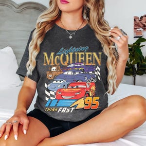 May include: A dark gray t-shirt with a graphic of Lightning McQueen and other Cars characters. The text "Lightning McQueen" and "Think Fast" are printed on the shirt. The number "95" is also printed on the shirt.