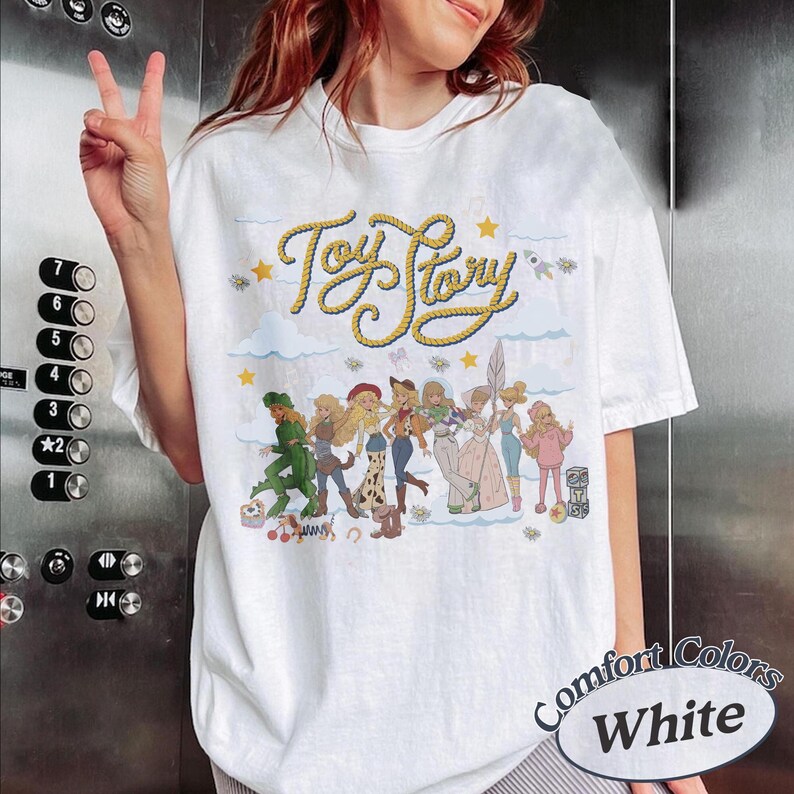 May include: A white short-sleeve t-shirt featuring the yellow rope-style text Toy Story at the top. Below the text is a graphic illustration of various characters from the Toy Story franchise, including Bo Peep in multiple outfits, set against a background of light blue clouds and small yellow stars.