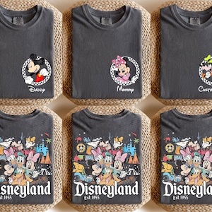 May include: Six dark grey t-shirts with Disney character designs. Three shirts feature Mickey, Minnie, and Goofy in circular frames with text. The other three shirts display a colourful Disneyland graphic with the text "Disneyland Est. 1955".